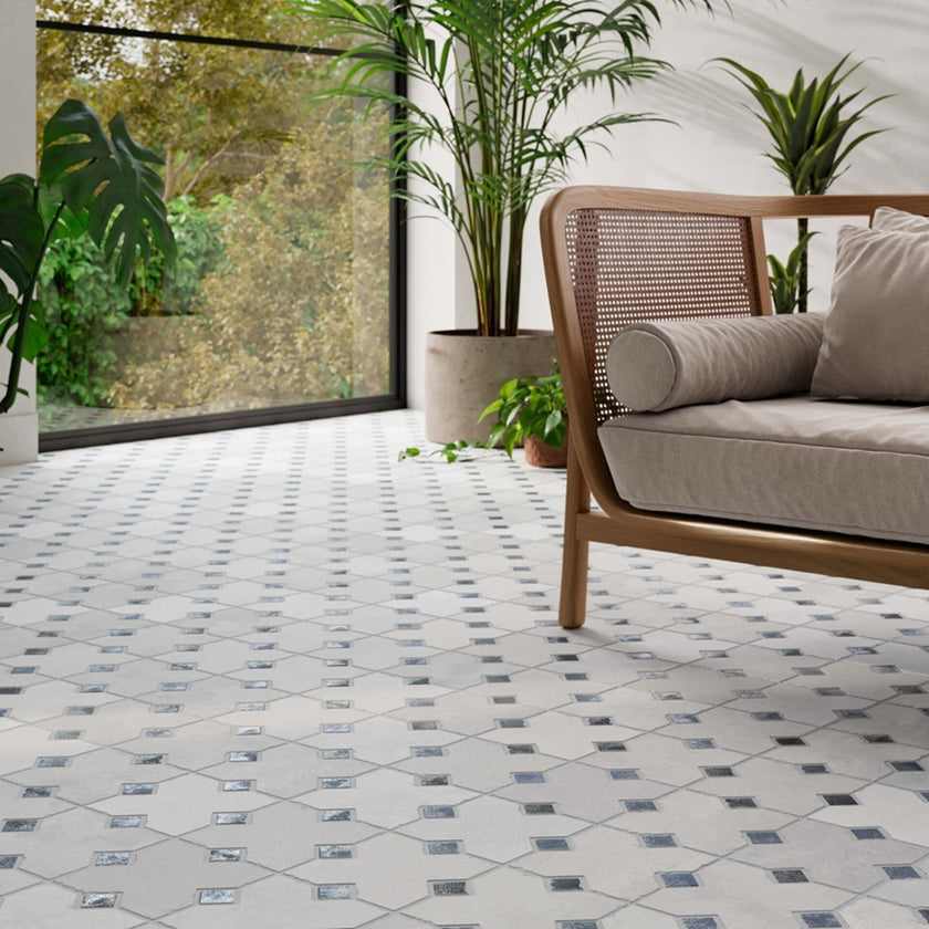 Carrelage Kurios Grey posé au sol dans un salon avec canapé en bois et plantes, motif gris clair à cabochons bleus et gris foncé