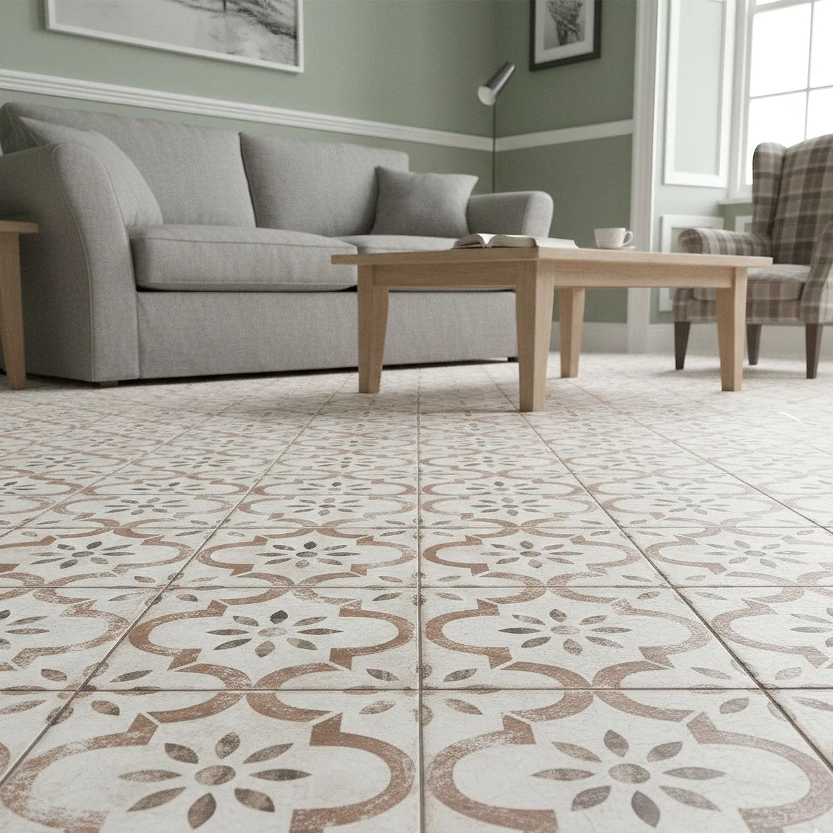 Salon avec sol en carrelage effet carreau de ciment Pre Leeds Cotto, à motifs floraux gris et terre cuite sur fond crème, canapé gris et table basse en bois.