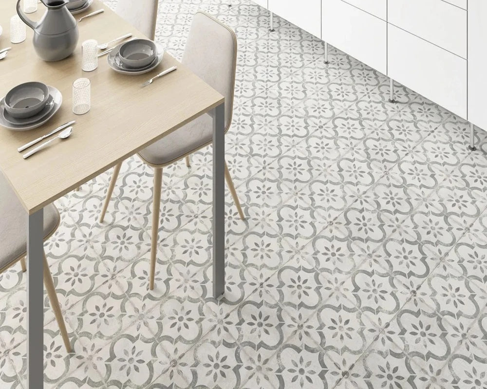 Cuisine avec sol en carrelage effet carreau de ciment Pre Leeds Musgo, à motifs floraux gris et vert sauge sur fond crème, table en bois clair et meubles blancs. 