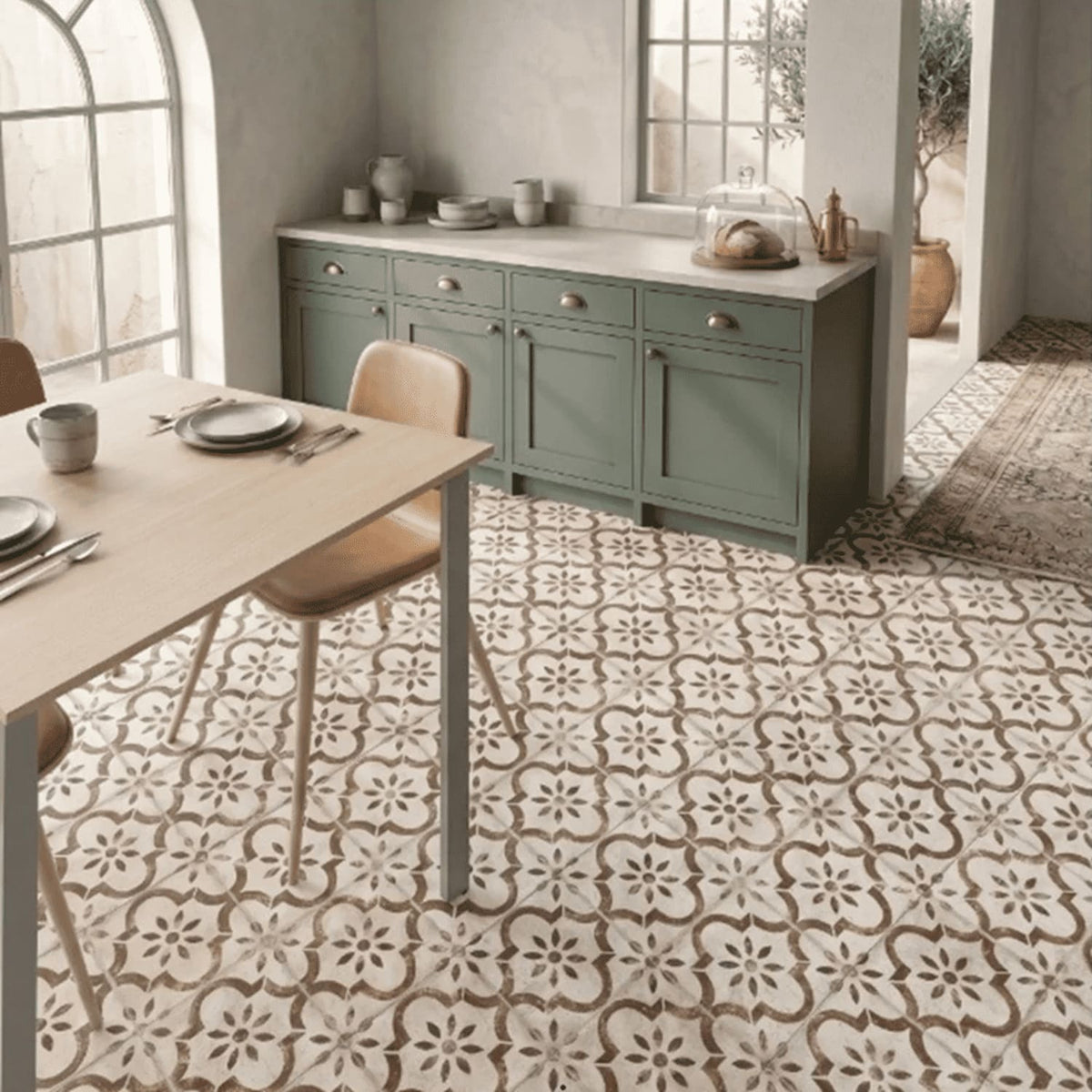 Cuisine avec sol en carrelage effet carreau de ciment Pre Leeds Cotto, à motifs floraux bruns sur fond crème, meubles vert sauge et table en bois.