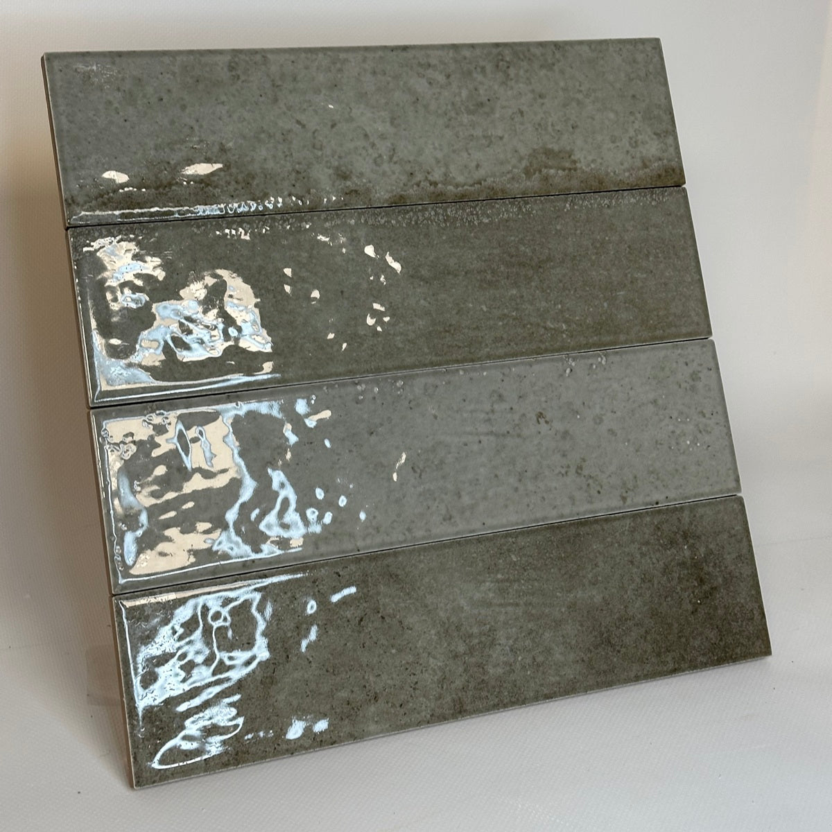 Vue inclinée de quatre carreaux effet zellige gris-beige, montrant leurs nuances et leur finition brillante.